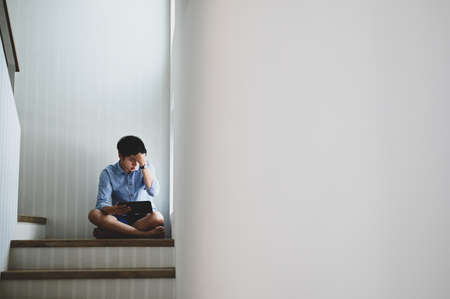 Sad and desperate man suffering depression problem sitting on staircase at home.の写真素材