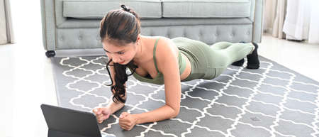 Young attractive doing yoga plank and watching online tutorials on laptop.