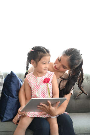 Mather and daughter sitting on sofa and using digital devices in living room at home.