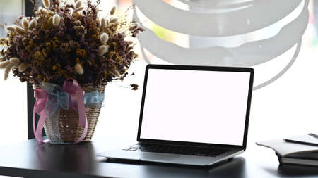 Modern workspace with blank screen laptop on white table and decorations in office.