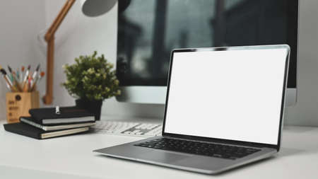 Modern workspace with blank screen laptop on white table and decorations in office.