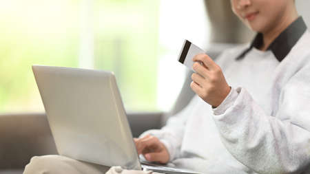 Cropped shot of young woman relaxing on comfortable couch while using laptop at home.