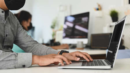 Cropped shot of man wearing medical facial mask working with computer laptop in the office.