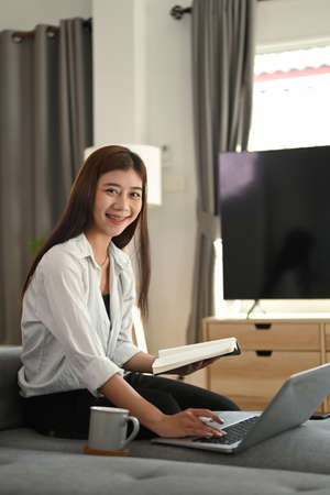 A young woman freelancer sit on couch in living room and working on laptop gadget at  home.