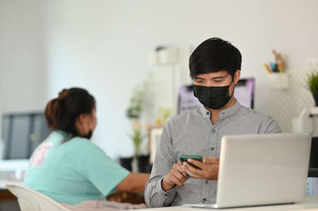 A young man photographer with face mask working with mock up laptop in comfortable workspace.