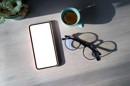 Top view of simple workplace with blank screen smart phone, glasses and coffee cup on wooden table.