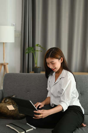 Portrait of an Attractive young woman using digital tablet and smiling while sitting on the sofa at...