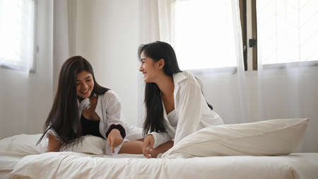 Asian lesbian LGBT Couple in white pajamas are using tablet while sitting in bed in bed room during vacations.の写真素材