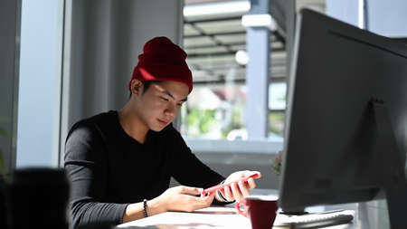 Portrait of a man graphic designer  in red wool hat working in creative office.