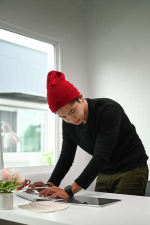 Portrait of a man graphic designer  in red wool hat working in creative office.