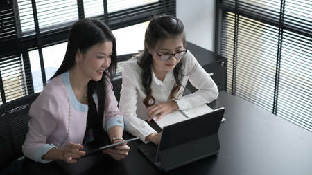 Businesswoman is using a digital tablet to discuss information with a younger colleague in a modern...