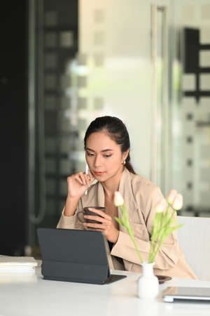 An experienced entrepreneur is reading some text on tablet while drinking coffee in office.の写真素材