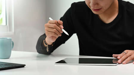 Side view of freelance graphic designer sitting at his workspace and looking at notebook while...