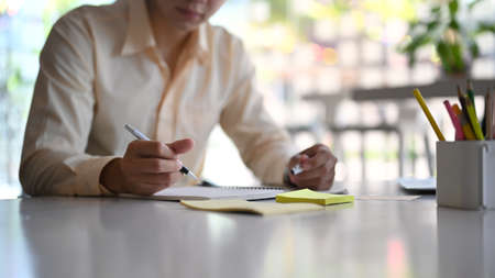 A businessman is working online with a laptop and writing down notes while sitting in a modern office.の写真素材