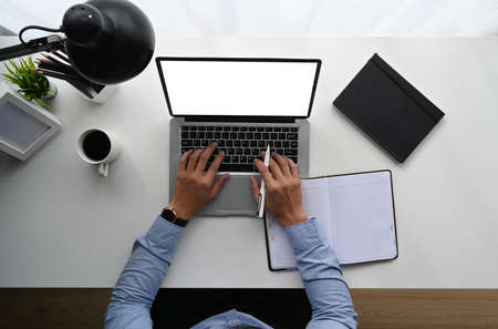 Top view of man is working on laptop while sitting at the white wooden desk.の写真素材