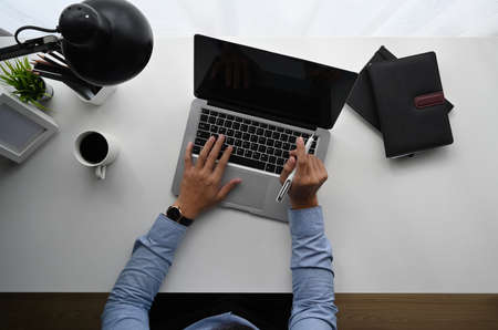 Top view of man is working on laptop while sitting at the white wooden desk.