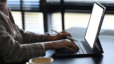 Close up view of young designer is sitting at workplace and using mobile phone with blank screen.