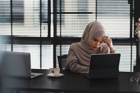 A happy muslim businesswoman in hijab is working on computer tablet at her office room.の写真素材