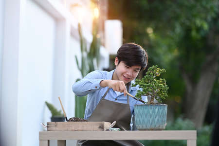 Portrait of a smiling man is trimming bonsai on wooden table at home. Hobby lifestyle concept.の写真素材