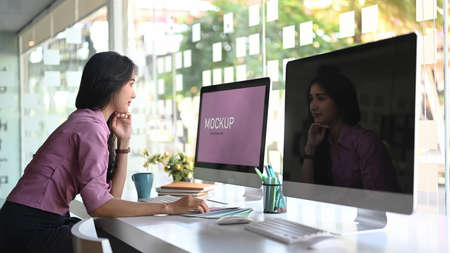 Side view of graphic designer artist working on multiple computer screens at modern office.の写真素材