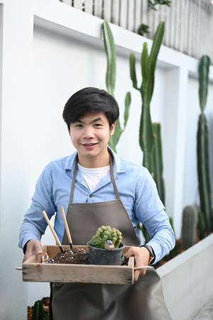 A young man gardeners hand transplanting bonsai in cement pots on the wooden table.  Home of...
