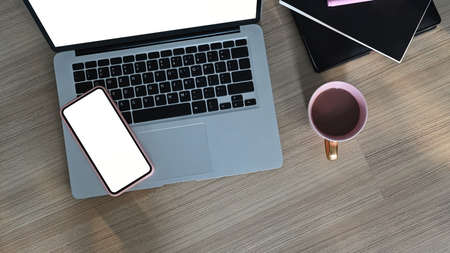Top view of freelancer workspace with blank screen laptop, mobile phone, coffee cup and notebook on wooden table.の写真素材