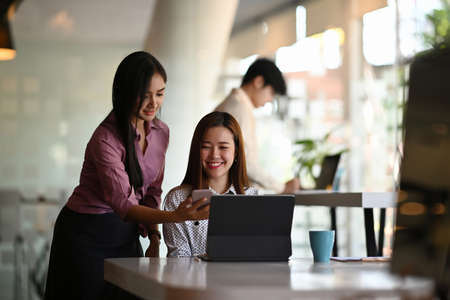 Two beautiful female mobile application designers are test and discuss new app features in meeting...