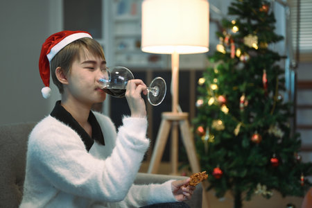 Close up shot of young woman playing guitar on sofa at home with Christmas tree in background.の写真素材