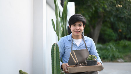 A youngman planting a bonsai tree into pot at home.の写真素材