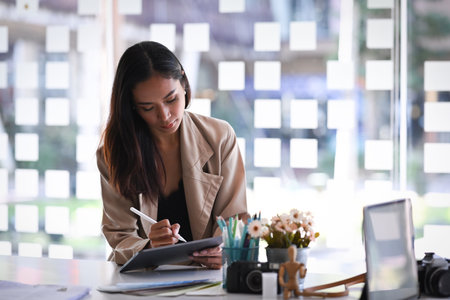 Smiling woman using computer tablet while sitting in modern office.の写真素材