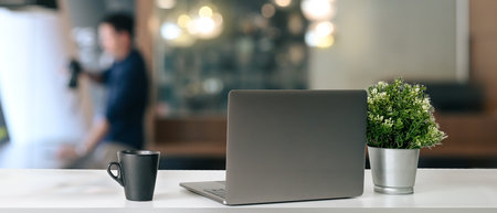 Modern workplace with open laptop placed on office desk with coffee cup and plant.