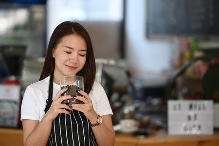 Young woman barista smelling and checking quality of coffee beans at coffee shop.の写真素材