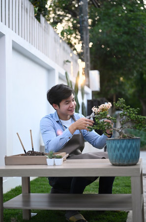 Portrait of cheerful male gardener in apron trimming flowers in pot with garden tools at his garden.の写真素材