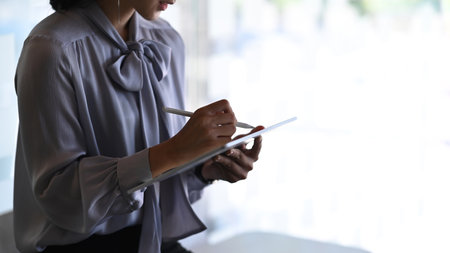 Cropped shot of businesswoman  hand holding stylus pen writing on digital tablet at modern office room.の写真素材