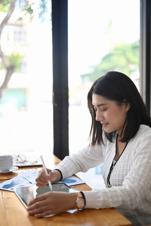 Side view of young woman sitting at wooden bar in coffee shop and using tablet computer.の写真素材