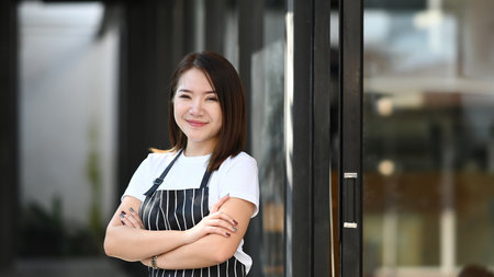 Portrait of young female entrepreneur smiling and standing with his arms crossed in front of her trendy cafe.の写真素材