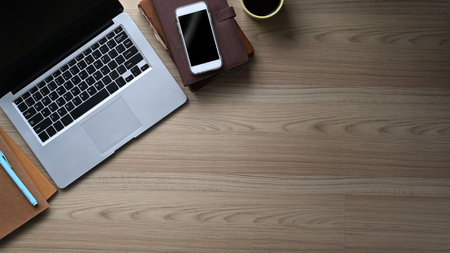 Top view of young designer hands holding digital tablet surrounded by stationery and coffee cup on...