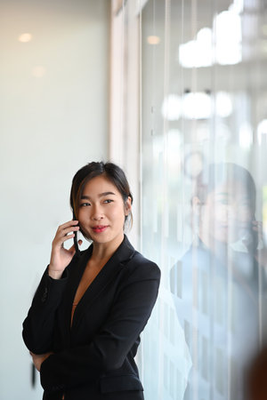 Portrait of confident businesswoman standing in modern office and talking on mobile phone.の写真素材
