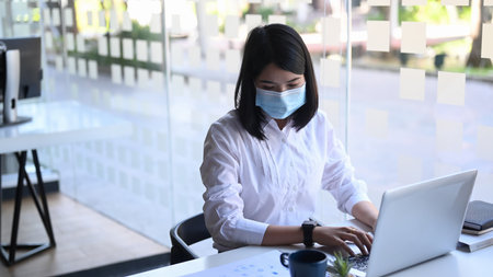 Young woman office worker in protective mask working or check information from website on her laptop at office.の写真素材