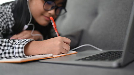 Close up view of Asian girl student during online courses on laptop computer while lying on sofa at home.の写真素材