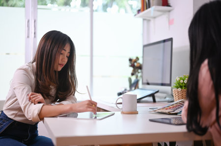 Portrait of young Asian graphic designer sitting at her workplace with serious face.の写真素材