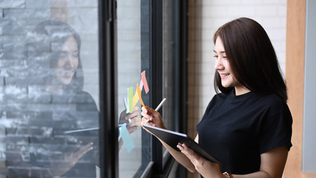 Business woman using digital tablet planning startup project and standing behind glass window with...