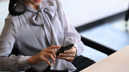 Cropped shot of young woman taking a break at her workspace checking her smart phone.の写真素材