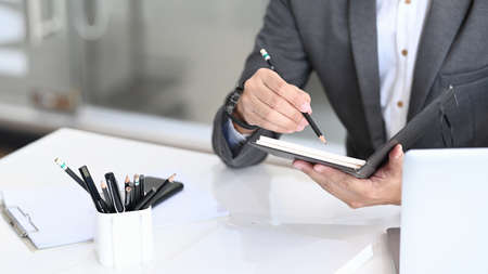Cropped shot of businessman in suit working with laptop computer and writing information on...