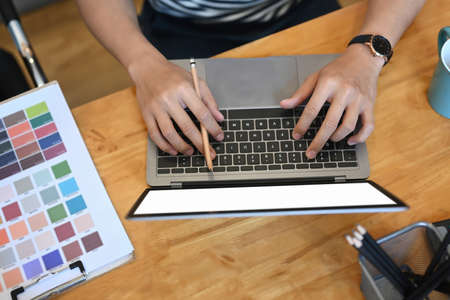 Overhead shot of young man designer working with laptop computer and color swatches on wooden table.の写真素材