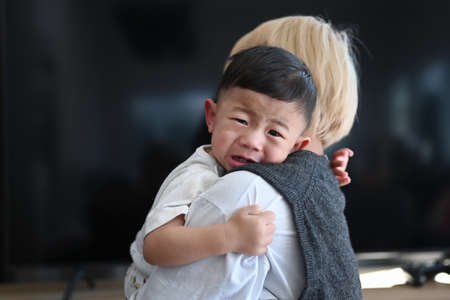 Young mother holding  her crying son at home.の写真素材