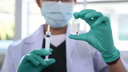 Close up view of female doctor holds syringe and bottle with vaccine. Clinical trial during pandemic.の写真素材