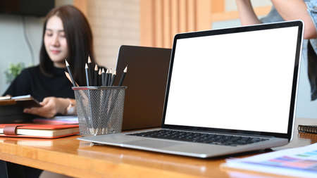 Young woman browsing websites on laptop and using mobile phone at office.