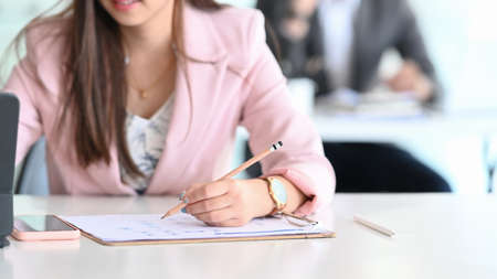 Cropped shot of businesswoman hands writing on business document and working with tablet computer.の写真素材