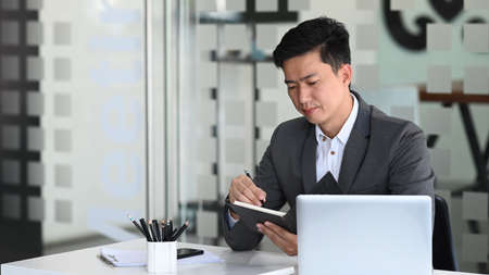 Businessman wearing protective mask working with tablet computer and analyzing business data on office desk.の写真素材